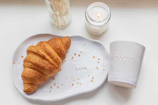 Photo white glass and a plate on which there is a fresh croissant made of clay with the inscription love handmade