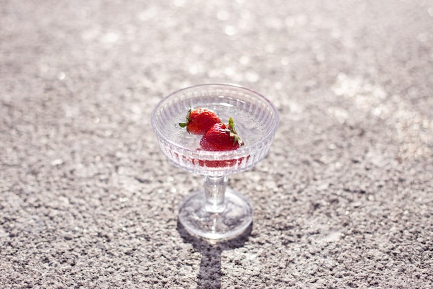 Bicchiere d'acqua bianco con fragola su sfondo grigio cemento