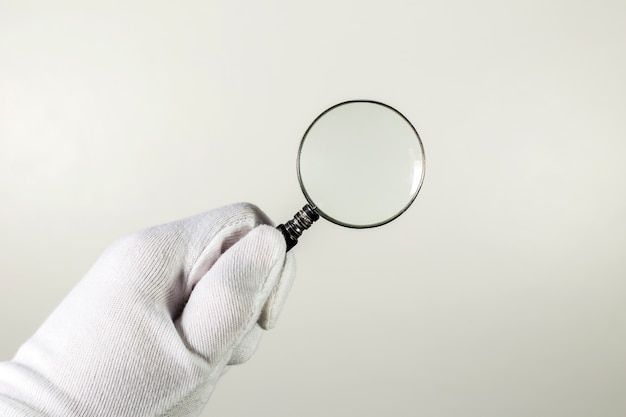 Photo white glove holding magnifier on the gray background.