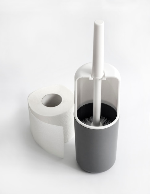 White and gray plastic toilet brush and roll of toilet paper on white surface