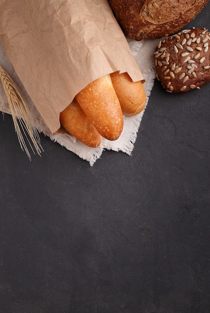 Pane bianco, grigio e di segale, baguette, rotolo con semi di sesamo su sfondo nero