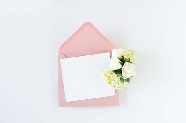 ピンクの封筒と白い背景の上のバラと白いグリーティングカード