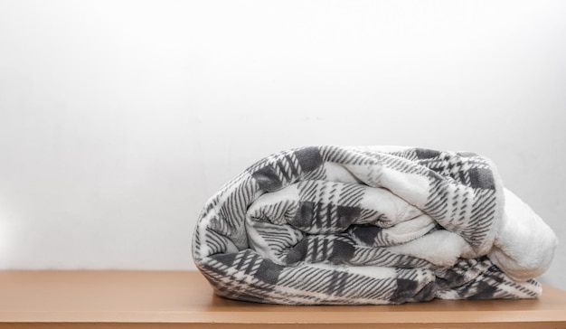 White and grey quilt with fur placed on a wooden table with copy space