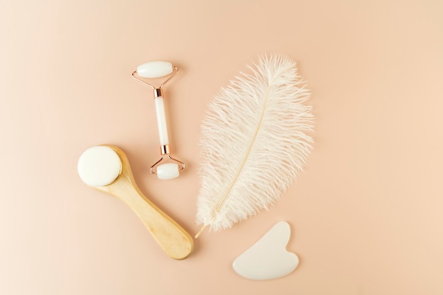 A white Guasha face massager a face roller and brush lying on a beige background