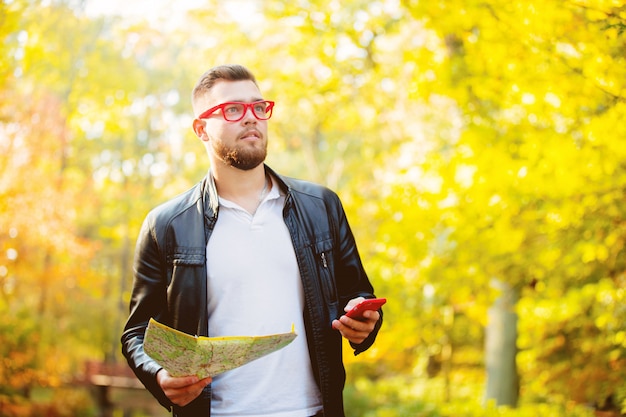 Ragazzo bianco con cellulare e mappa in un parco