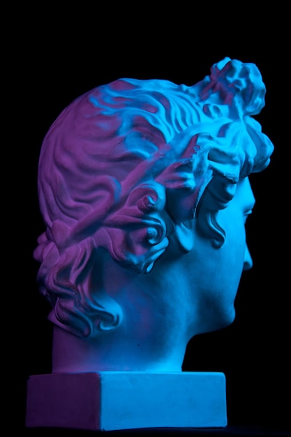 White gypsum copy of ancient statue of Apollo God of Sun head for artists isolated on a black background. Plaster sculpture of man face. Toned blue and purple.