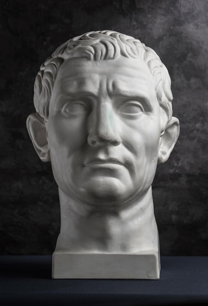 White gypsum copy of ancient statue of Guy Julius Caesar Octavian Augustus head for artists on a dark textured background. Plaster sculpture of man face.