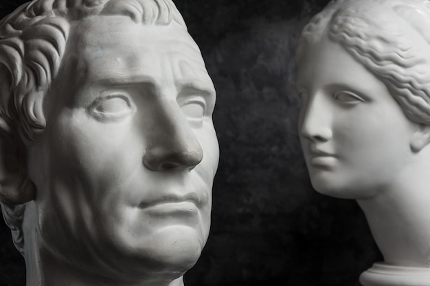 White gypsum copy of ancient statue of Guy Julius Caesar Octavian Augustus and Venus head for artists on a dark textured background. Plaster sculpture of statue face.