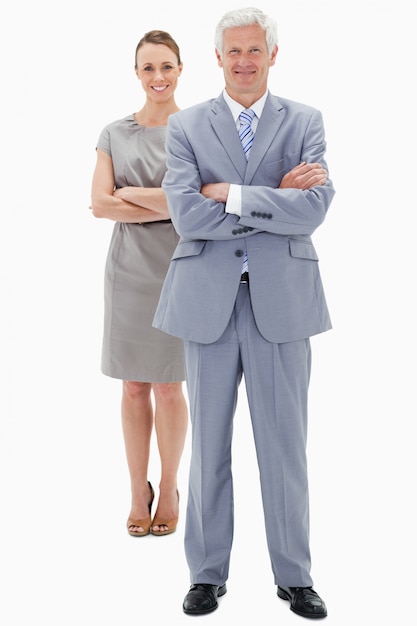 White hair businessman with a woman in background smiling and crossing their arms