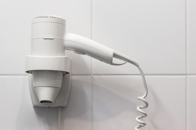 White hair dryer on the wall in bathroom with white tiles