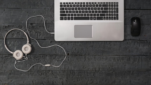 White headphones, mouse and laptop on a wooden background. The concept of workplace organization. Equipment for recording, communication and listening to music. Flat lay.