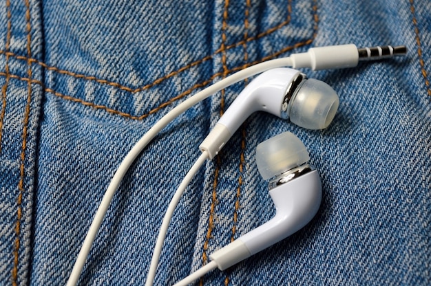 White headphones for the phone on the background of a denim jacket. close-up.