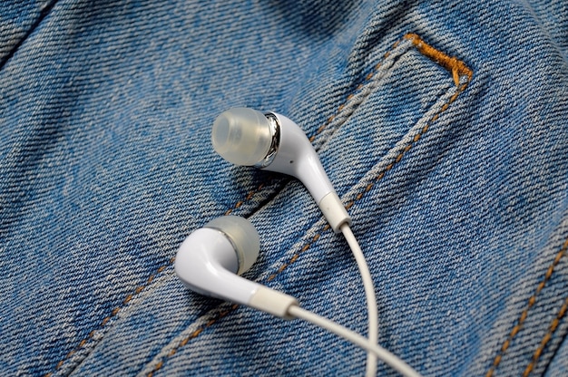 White headphones for the phone on the background of a denim jacket