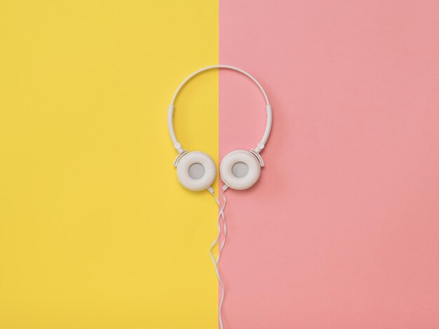 White headphones with a wire on a yellow and pink background. Mobile audio playback equipment.