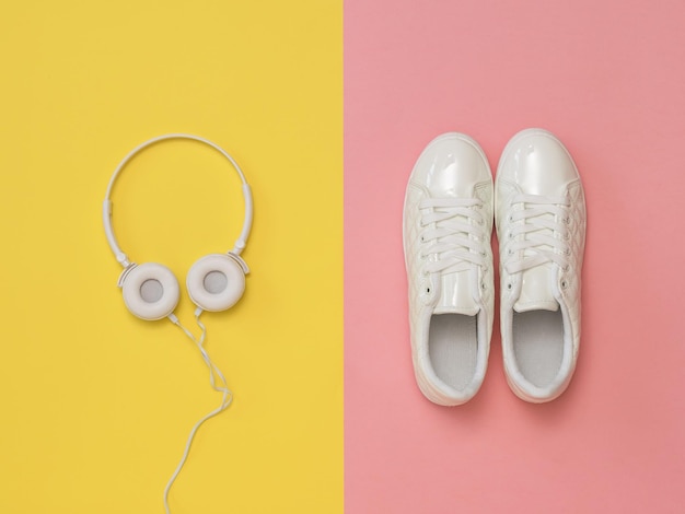 White headphones on a yellow background and white sneakers on a pink background The concept of a healthy lifestyle and music