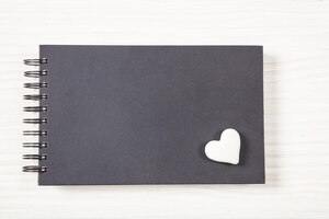 White heart on a black notebook top view isolated and copy space on a white wooden background
