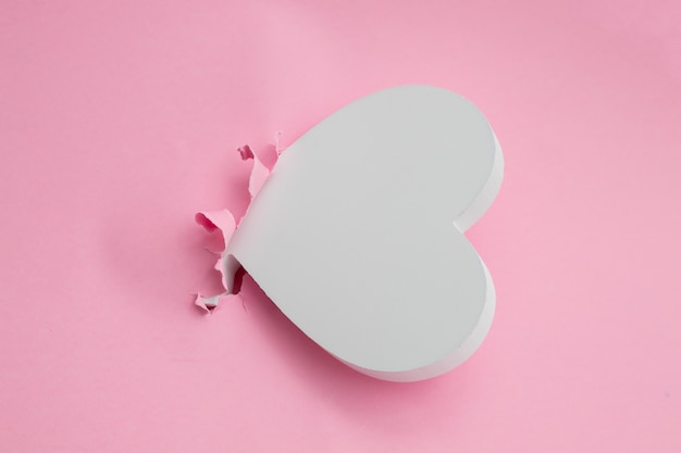 White heart making hole in pink paper background