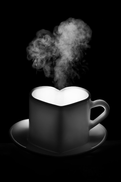 A white heartshaped mug with a warm drink and curly steam in the shape of a heart on a black background