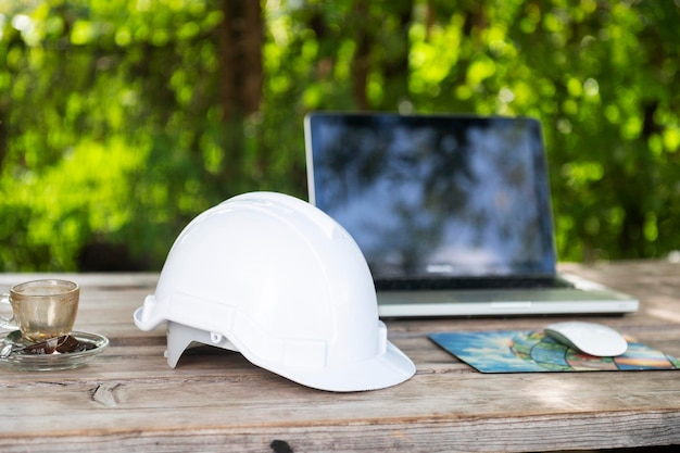 White helmet and computer at cafe with sunlight background\
engineer view sitting construction planning