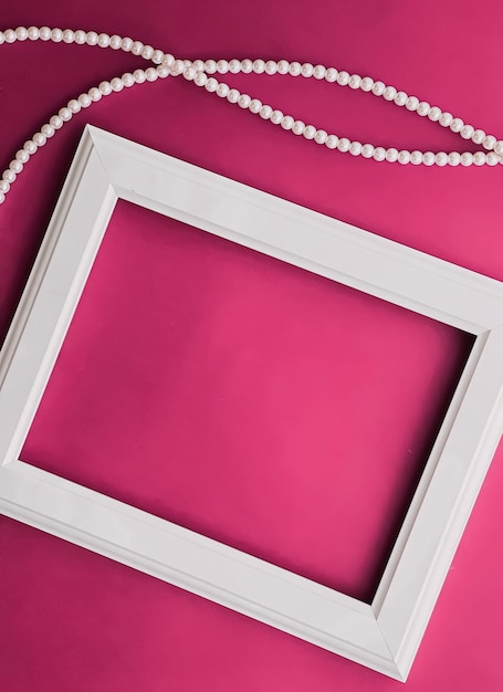 White horizontal art frame and pearl jewellery on pink background as flatlay design artwork print or photo album