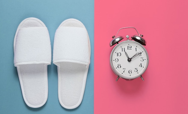 White hotel sleeping slippers and alarm clock on colored