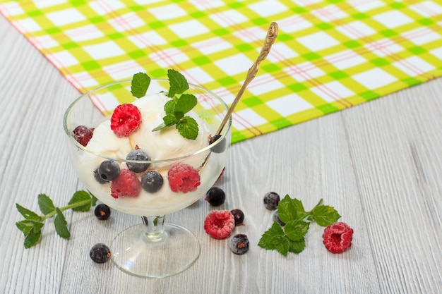 White ice cream in a glass with raspberry and currant berries\
and mint leaves on checkered napkin