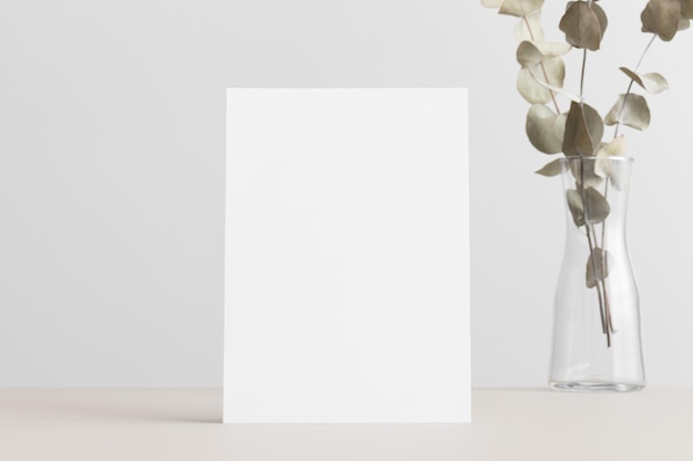 White invitation card mockup with an eucalyptus on a beige table 5x7 ratio similar to A6 A5