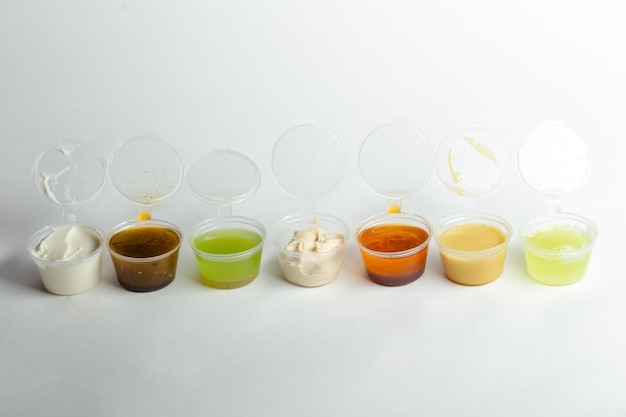 Photo white isolated background, different types of sauces and colors in plastic open containers.