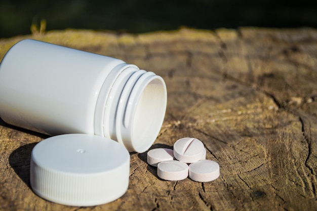 White jar and white pills lie on a stump Pills or tablets closeup with bokeh Concept photo on theme Coronavirus and Covid19