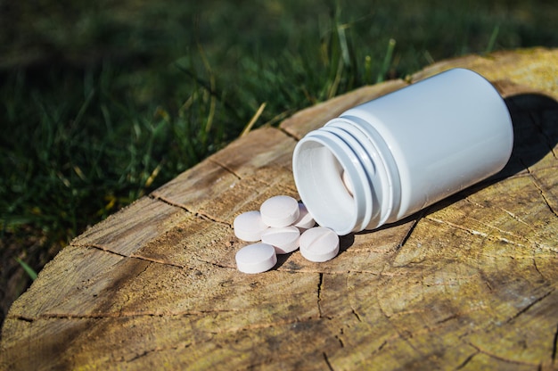 White jar and white pills lie on a stump Pills or tablets closeup with bokeh Concept photo on theme Coronavirus and Covid19