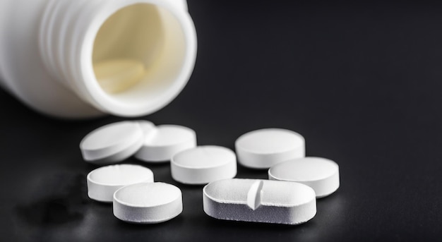 White jar with watered pills on black background drugs and drugstore concept