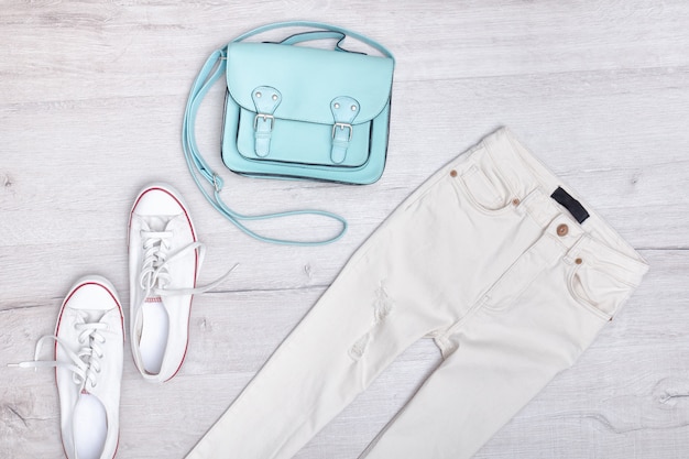 白のジーンズとスニーカー、ミントバッグ。ファッショナブルなコンセプト。木製の背景。