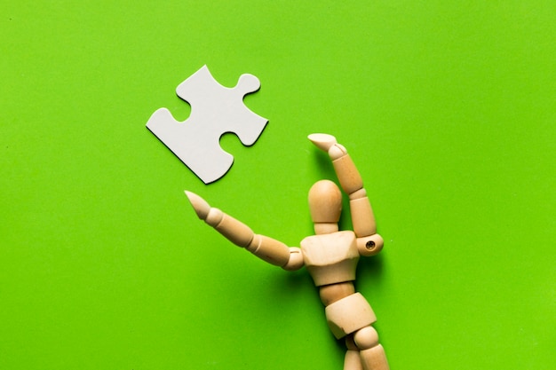 White jigsaw puzzle piece and wooden human figure over green surface