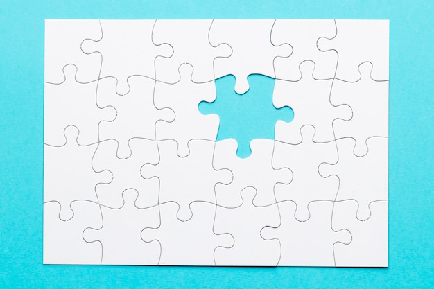 White jigsaw puzzle with one missing piece on blue backdrop