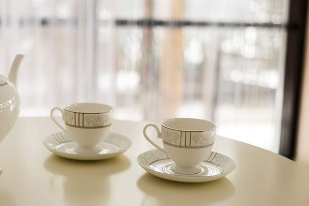 White kettle and two cups for tea on the table.