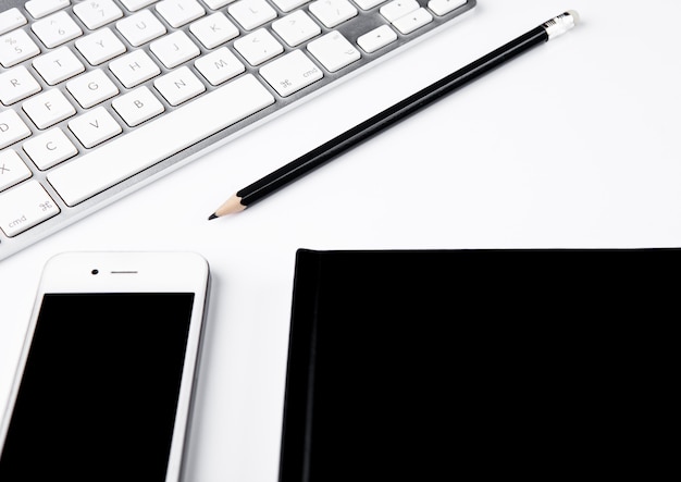 White keyboard with black pencil and phone on desk on white surface