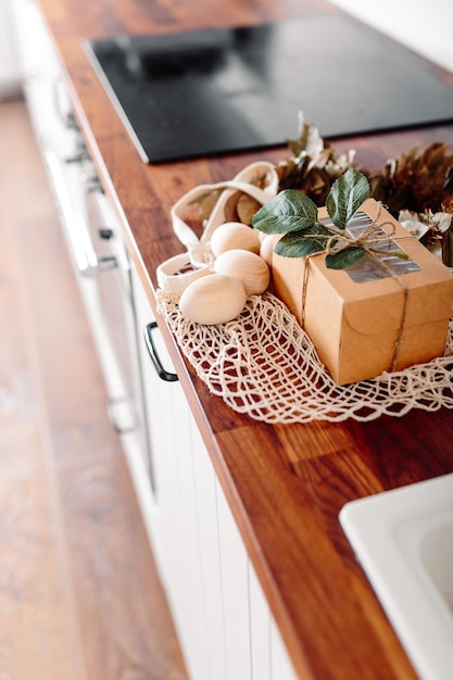 Фото Белая кухня с яйцами и подарочной коробкой пасхальная открытка с деревянными яйцами сетчатый покупатель с яйцами