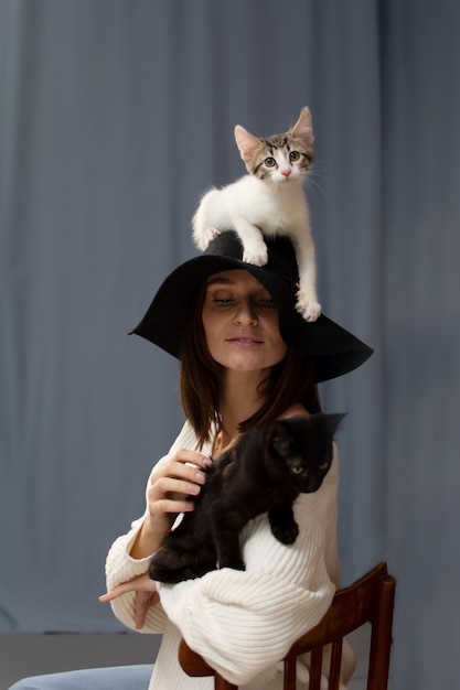 A white kitten is sitting on the hat with a large brim head of a young woman