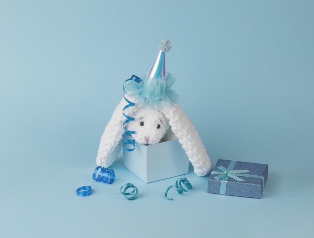 Un coniglietto bianco lavorato a maglia che spunta da una confezione regalo su sfondo blu.