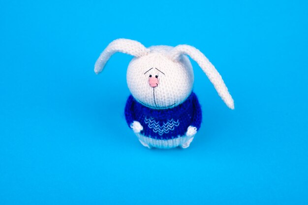 White knitted rabbit, in a blue jacket with a heart, on a blue background. rabbit with a heart. place for writing