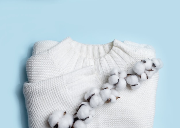 White knitted sweater and branch of cotton on light blue