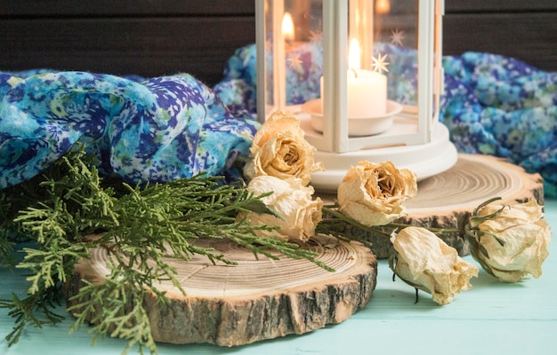 White lantern and dried roses with juniper branches. White candlestick on a wooden background
