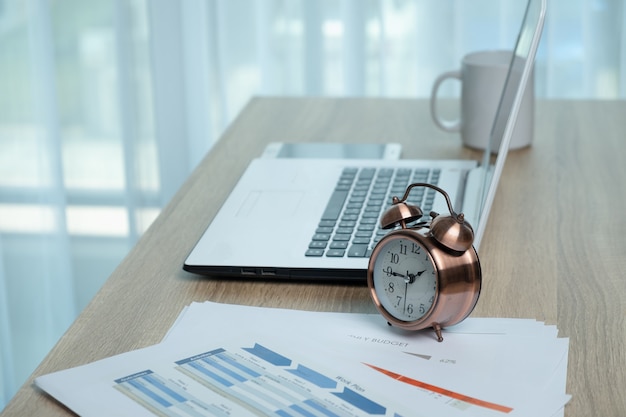 Photo white laptop and alarm clock on the desk