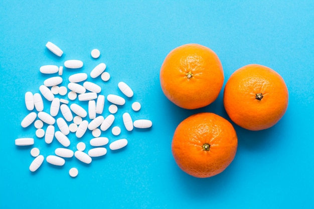 White large oval pills and ripe oranges on a blue background. Medicines and synthetic vitamins. The concept of choosing medicines and natural fruits. Top view