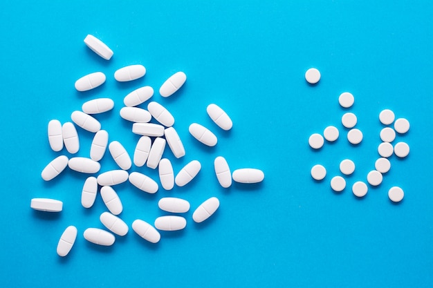 White large oval and small round pills are scattered on blue.