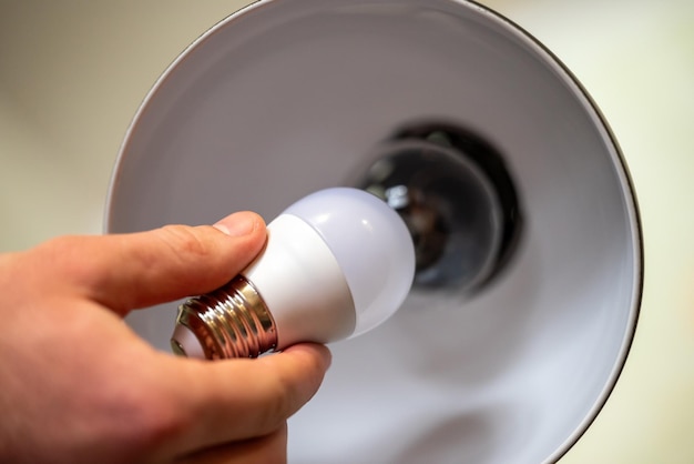 White LED light bulb in males hand holding it near the the lamp with incandescent bulb