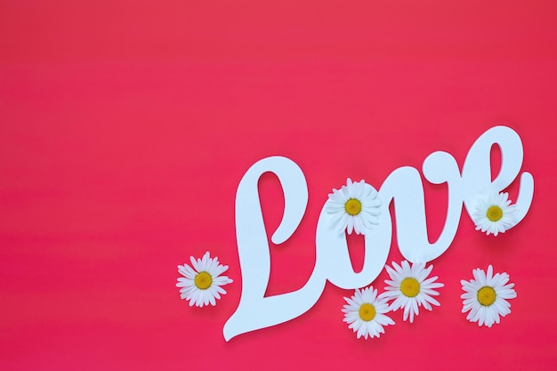 White letters forming word LOVE written with chamomile flowers on pink background St Valentine's Day wedding holiday concept