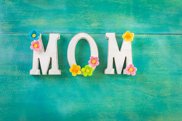 White letters MOM on a painted wood background.