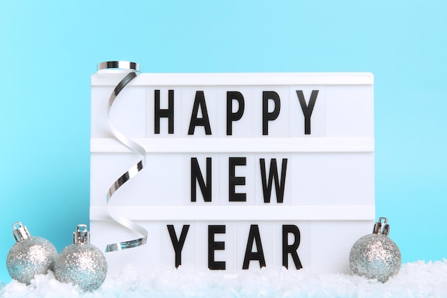 White lightbox with text Happy New Year and Christmas balls on a table with snow Minimal Christmas or New Year concept