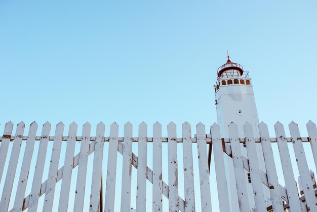 white lighthouse with white fence on blue sky background near the sea